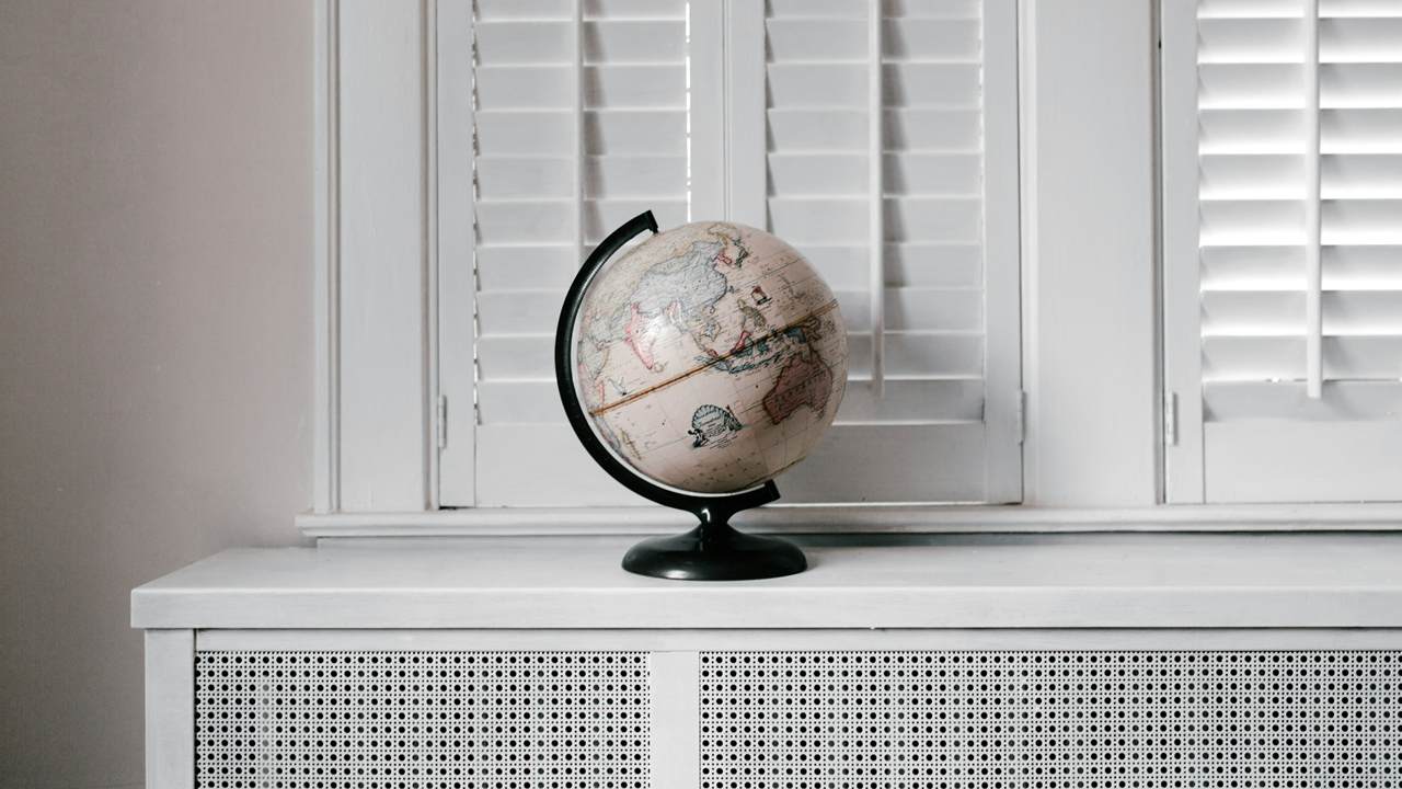 A small desk globe turned to show Asia and Australia stands on a white cabinet in front of white window shutters.