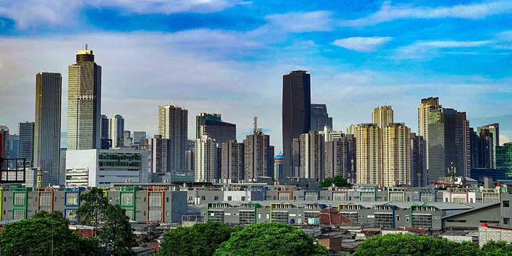 The Jakarta skyline under a deep blue sky with scattered clouds.