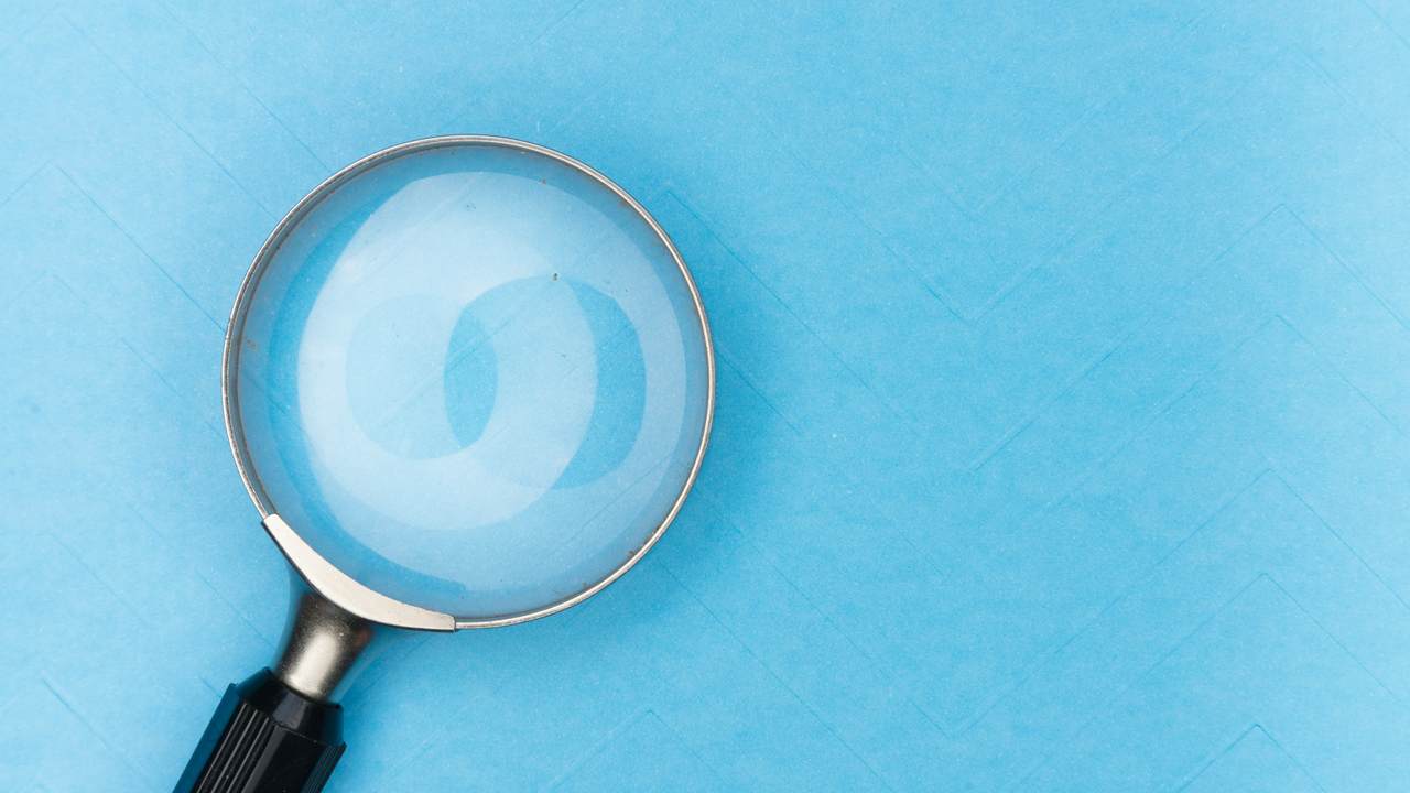 A magnifying glass with a black handle lies on a sheet of light blue paper.