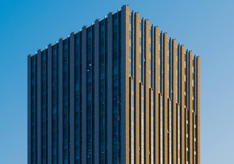 The upper floors of a modern high-rise with vertical gold and navy fins against a clear blue sky.