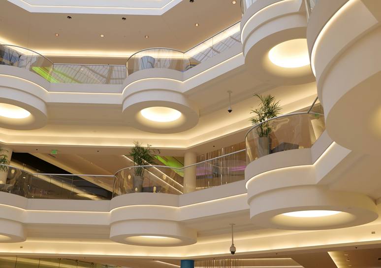 Curved cream balconies with glass railings and potted palms in the atrium of a multi-storey shopping mall.