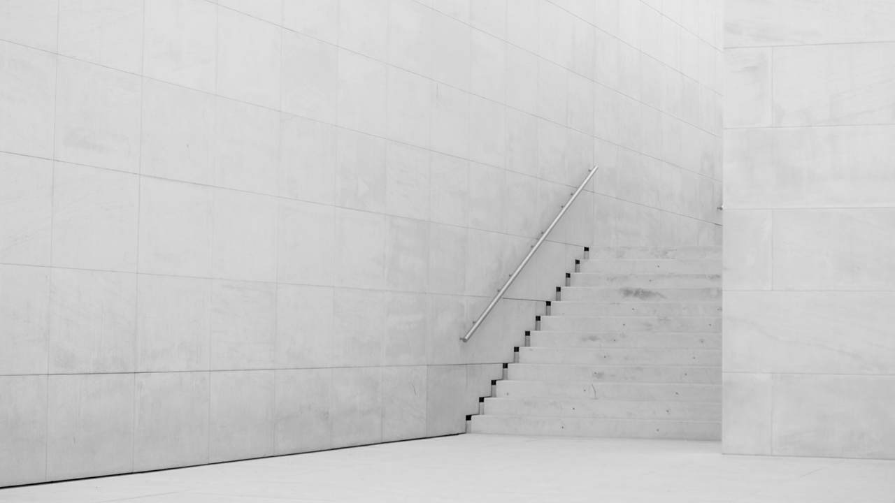 A flight of pale concrete steps with a steel handrail rises beside a tall white panelled wall.