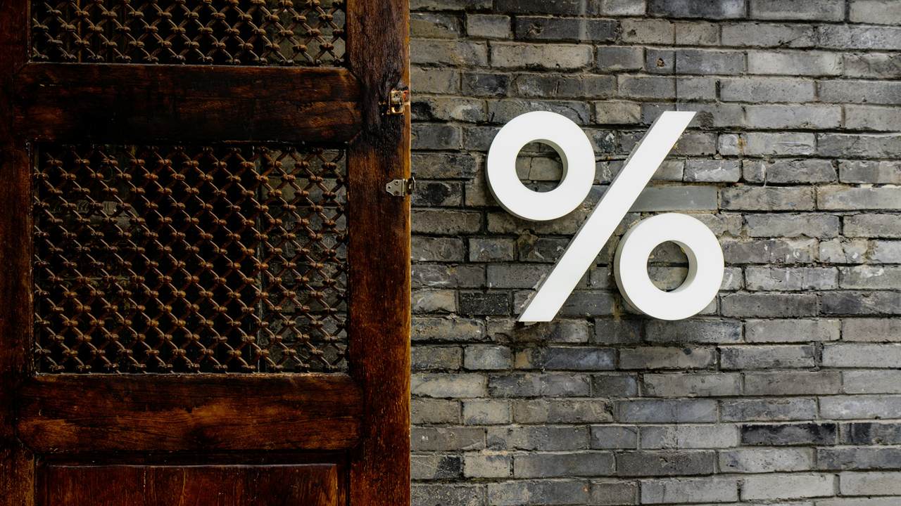 A large white percent sign is mounted on a grey brick wall next to a dark wooden door with lattice panels.